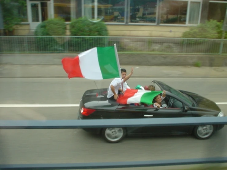 two people are riding in a convertible car with italian flags