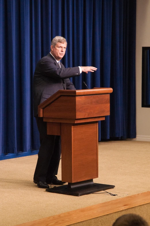 a man in a suit stands at a podium while giving a speech