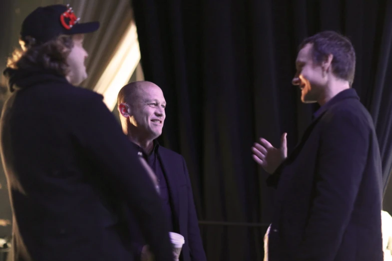 three men laugh and talk while wearing headphones