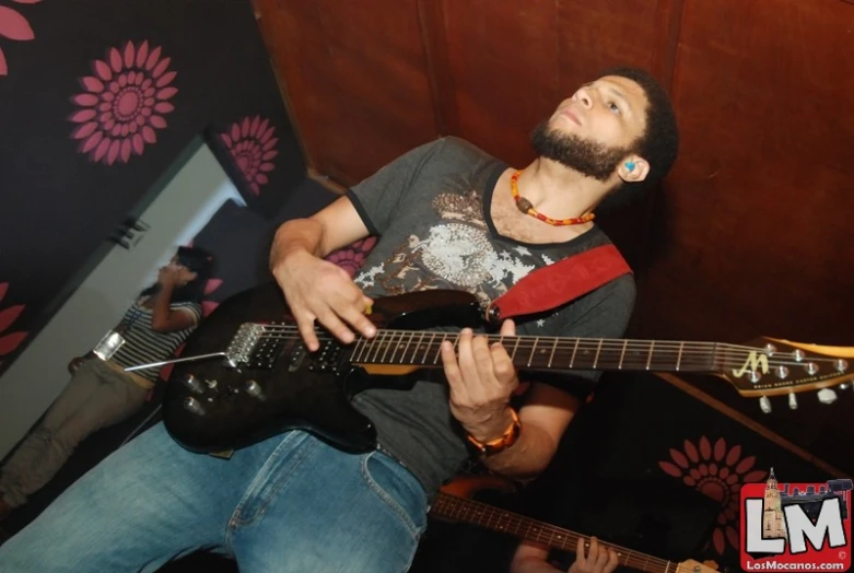 a man in a gray shirt playing on a black guitar