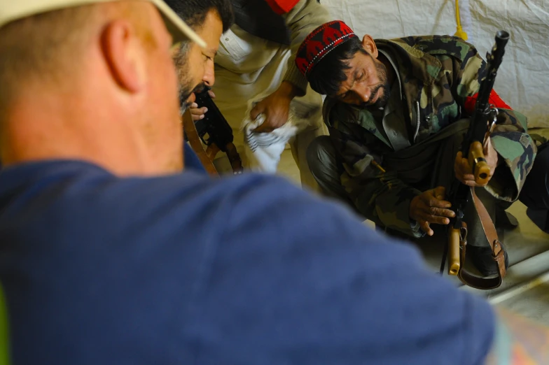 an older man kneeling down next to another man with a rifle