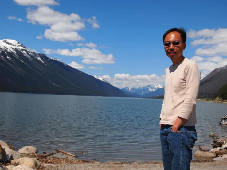 a man standing by a large lake in front of some mountains