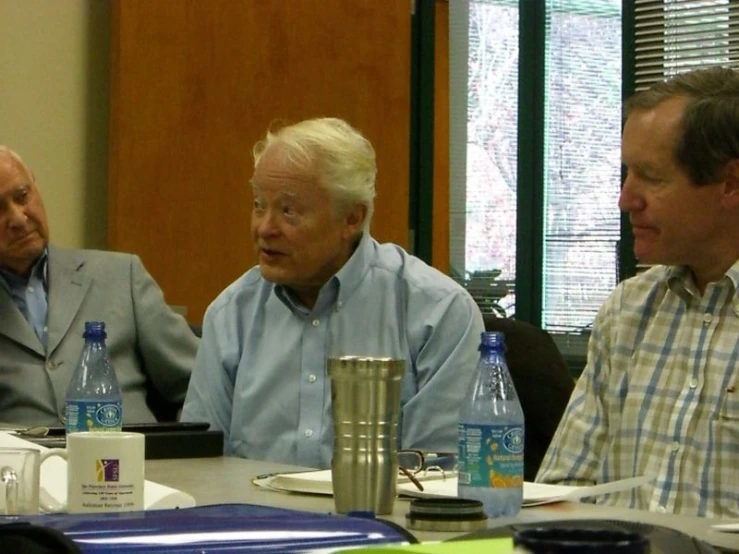 four older men sitting at a conference table with water bottles