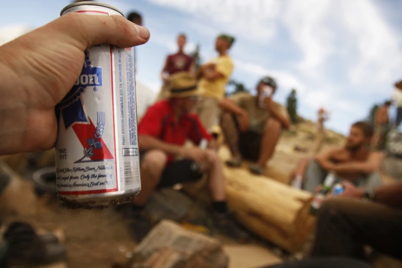 a hand holding a beer in a group of men