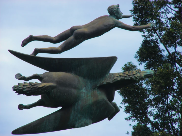 two statues of a young man diving with a large tree in the background