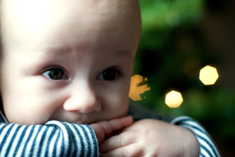 the baby in front of a christmas tree is holding it's hands up to his face