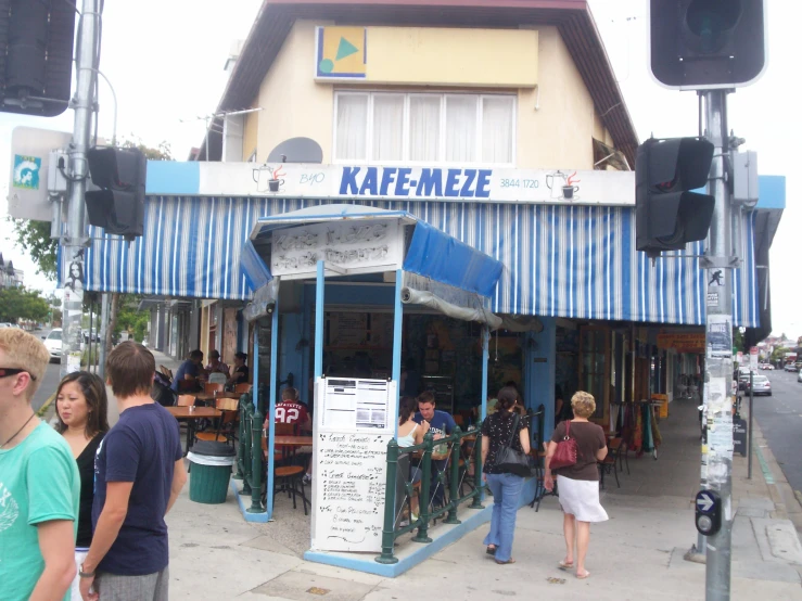 people are standing outside of a building with a small blue and white awning