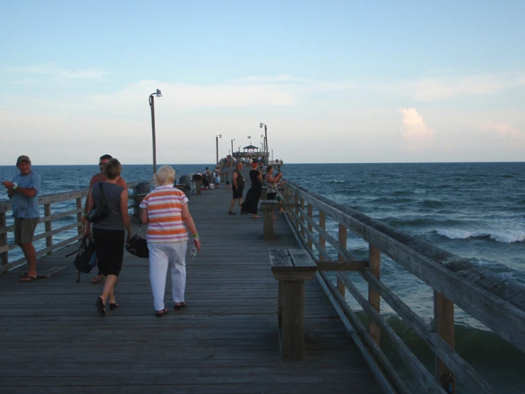 many people are walking along a wooden pier on the ocean