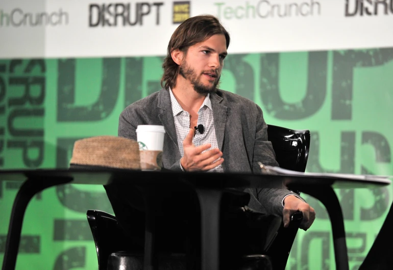 a bearded man in a grey jacket sitting on top of a black chair