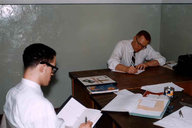 two men are seated at a desk with papers