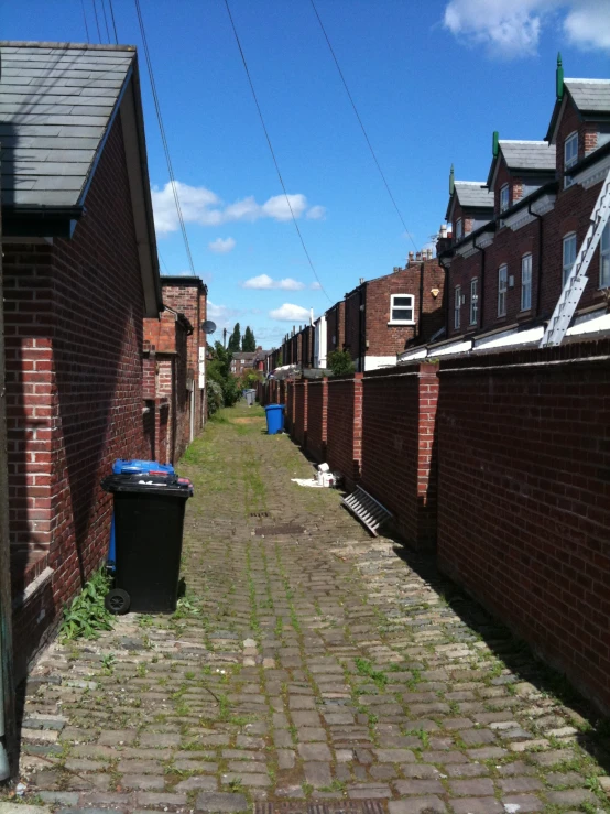 a narrow street with a blue garbage can between brick buildings