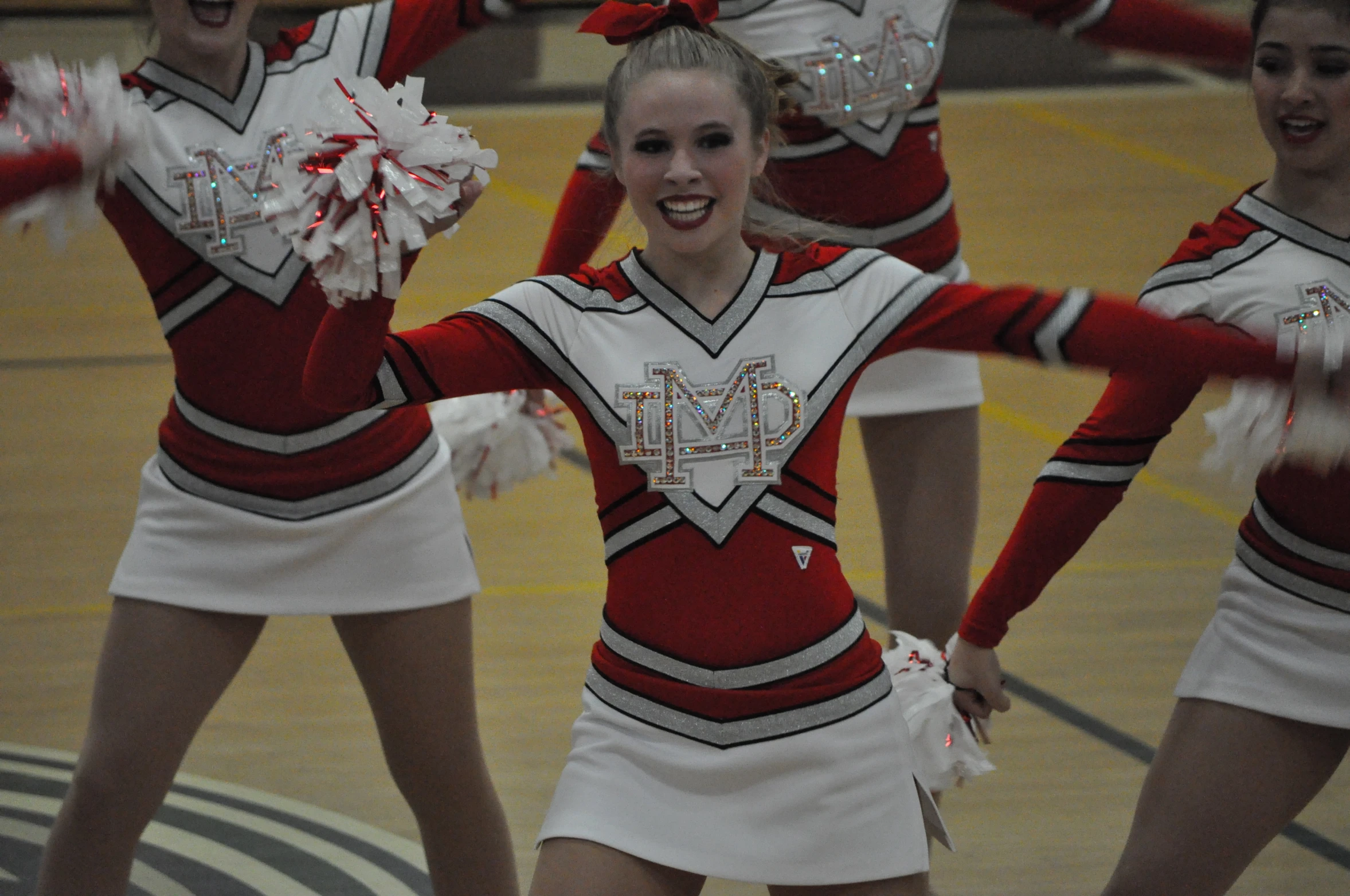 cheerleaders dressed in red and white stand in a gymnasium