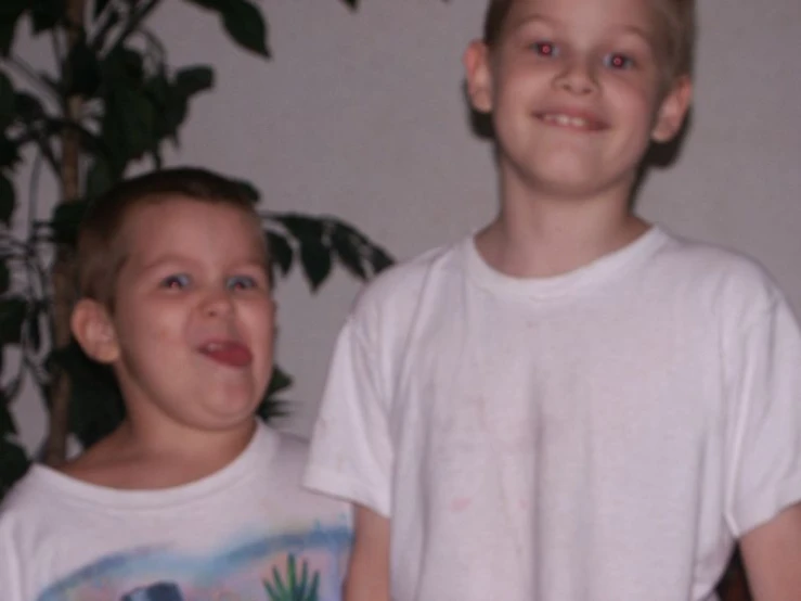 a little boy in white shirt holding a banana with another  looking on