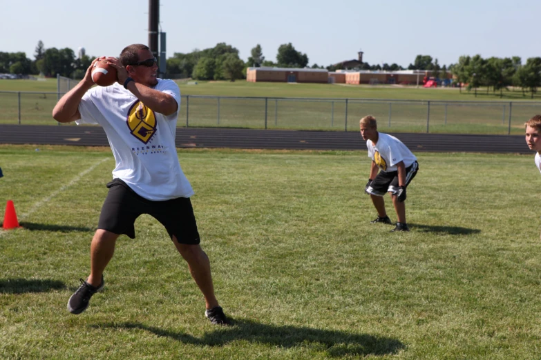 two guys wearing white shirts and black shorts are playing catch