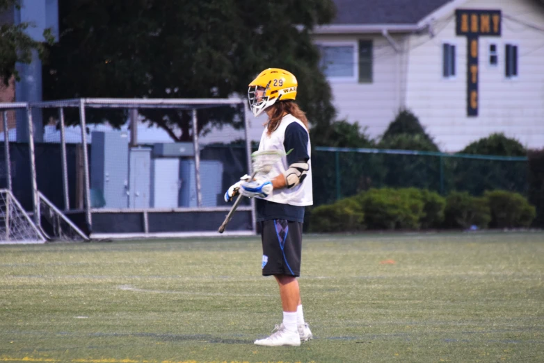 a young woman with a yellow helmet holding a lacrosse stick