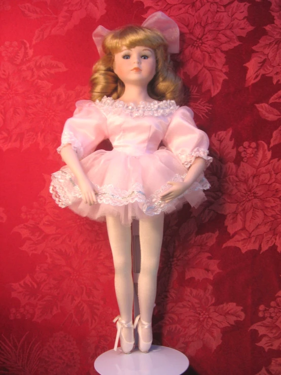 the doll is dressed in pink, wearing a tutu and holding on to a leg