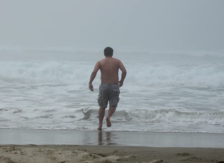a shirtless man runs along the edge of a wave covered beach