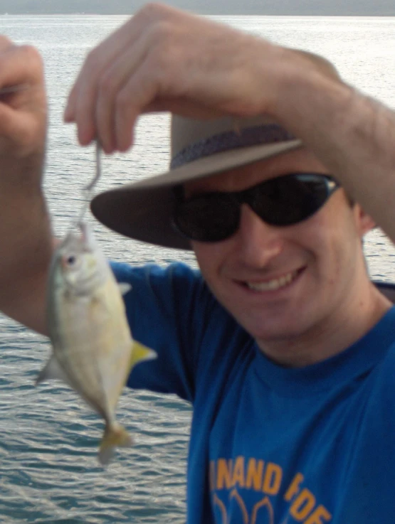 a man in a hat holding up a small fish