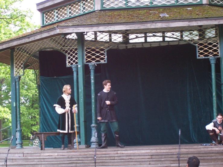 three people standing on top of a stage near a gazebo