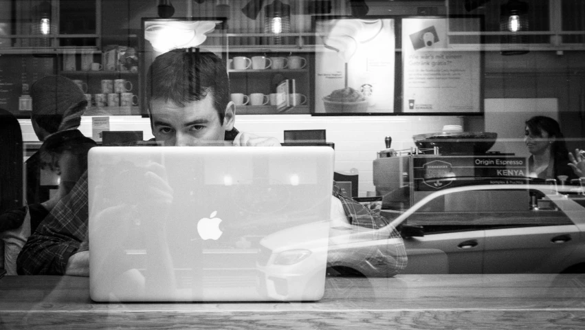 a man working on a laptop while behind a glass