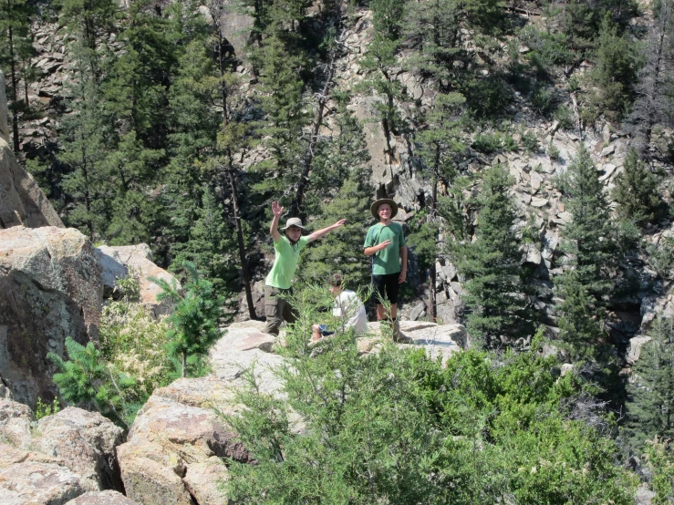 three people standing on rocks high above trees