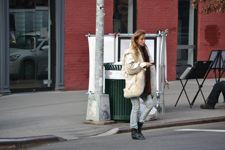 a young woman in fur coat next to sidewalk area with red building in the background