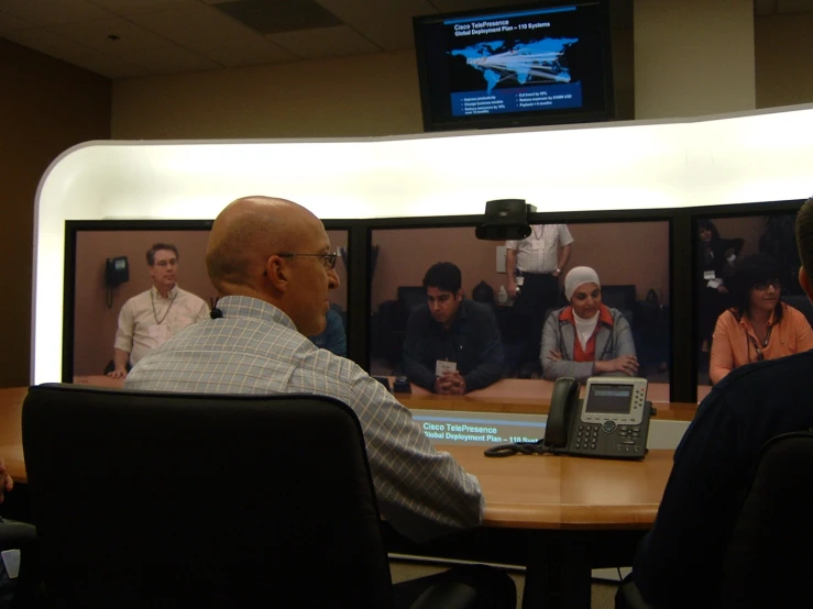 a man in front of four television screens watching some men on a phone