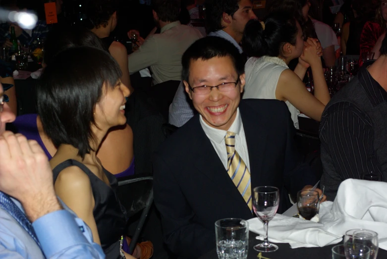 smiling man with glasses and suit coat next to two woman