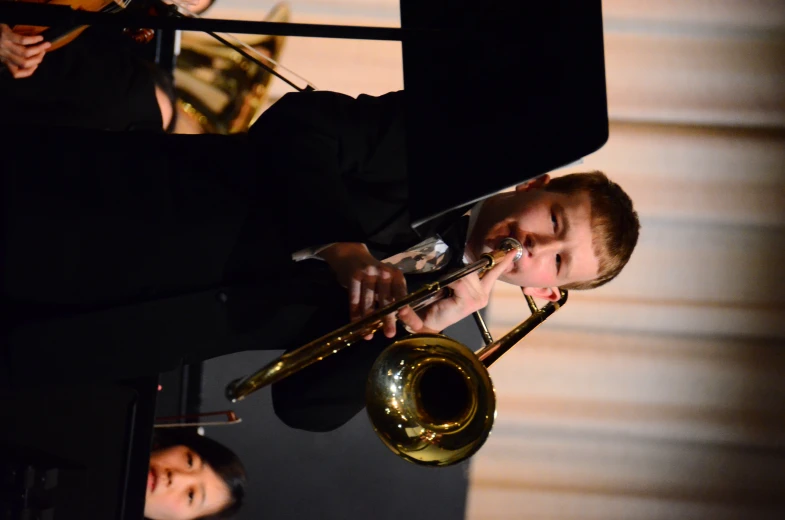 a young man plays the trumpet while other people watch from behind him