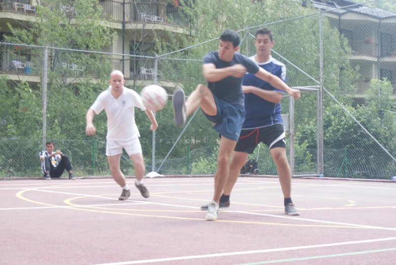 three men play with soccer on an outdoor court