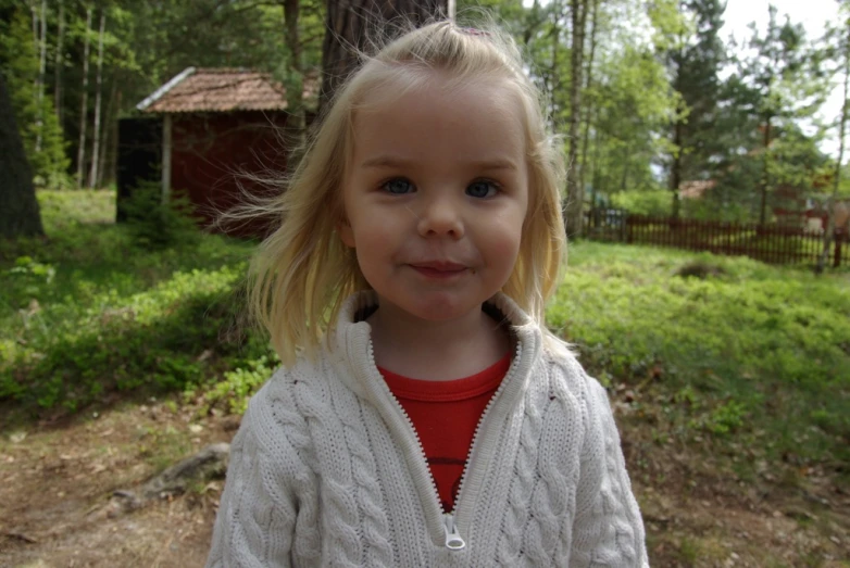a girl in a cardigan standing near a forest