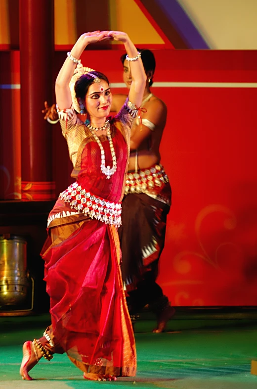 a woman in a sari dances on stage with other dancers