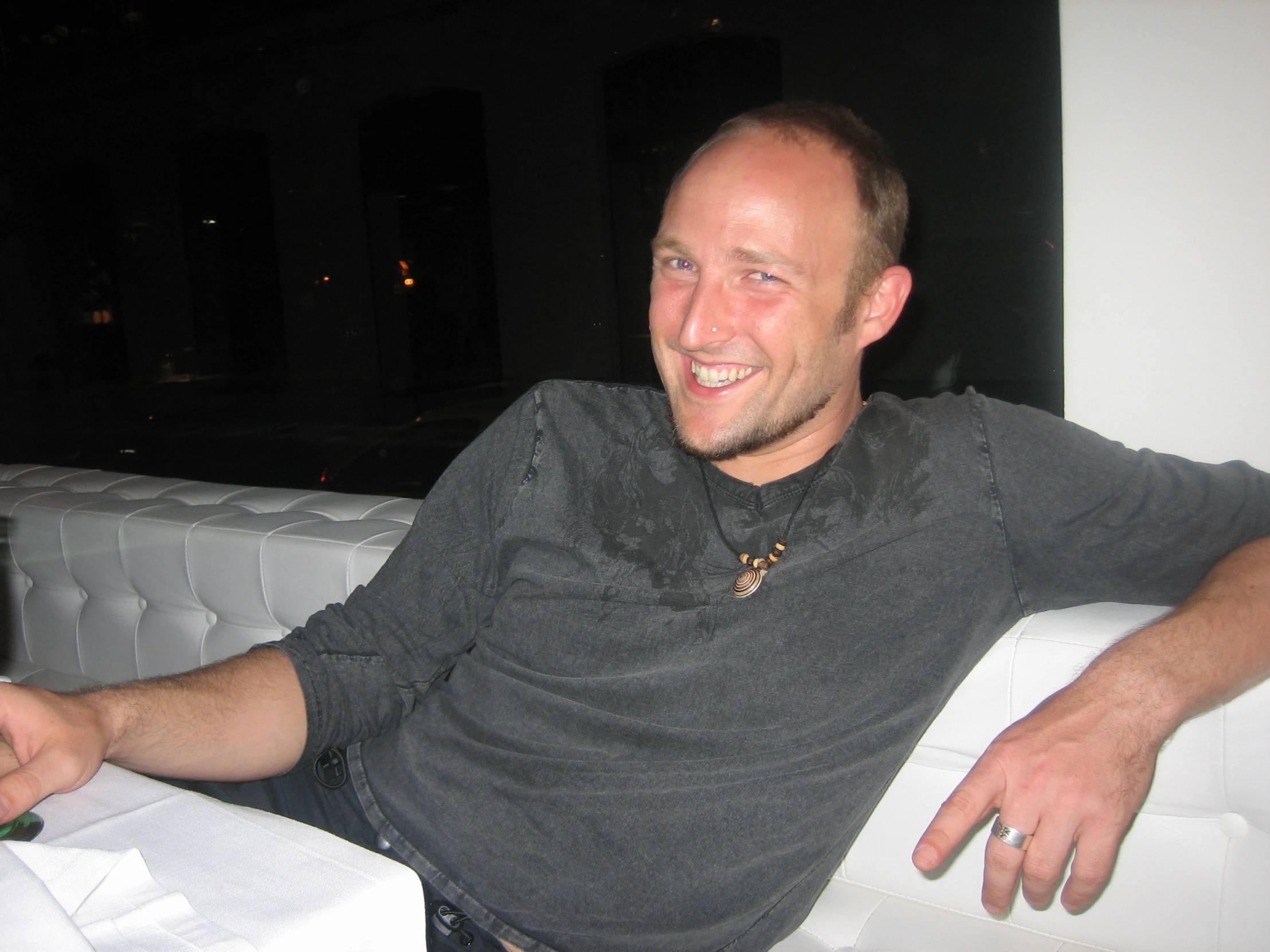 a smiling man sitting on top of a chair next to a bottle