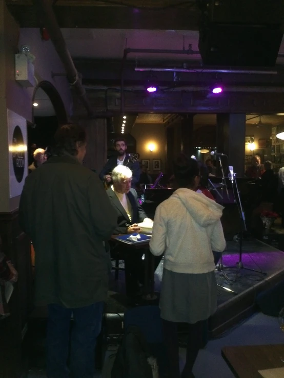 a woman standing at a piano with a bunch of people