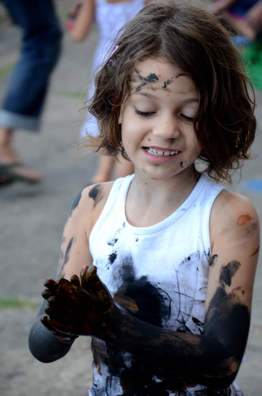 a little girl covered in black paint holding a piece of food