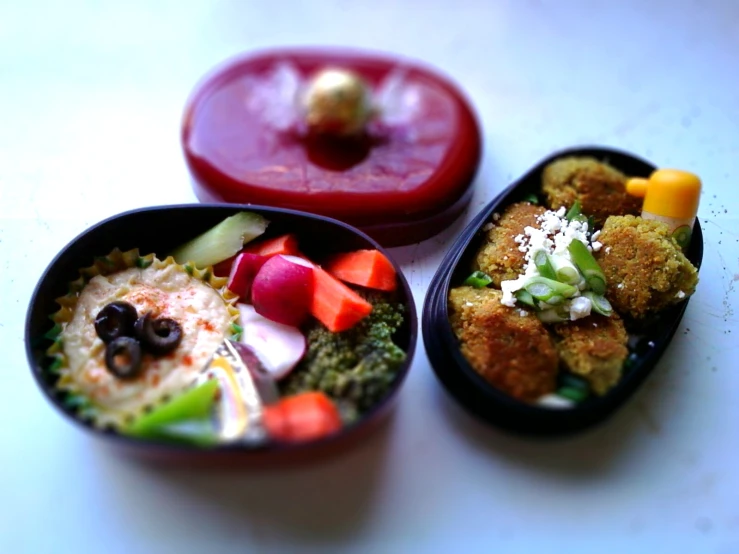 three small black and red containers containing different food items