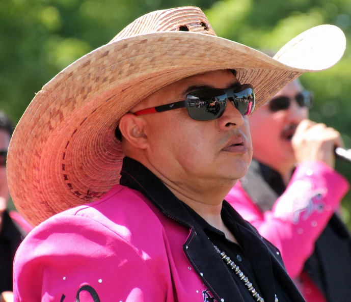 a man in a pink shirt and cowboy hat looks off to the side