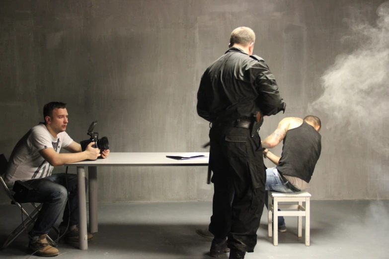 a man in black leathers shooting another men smoke in a black office