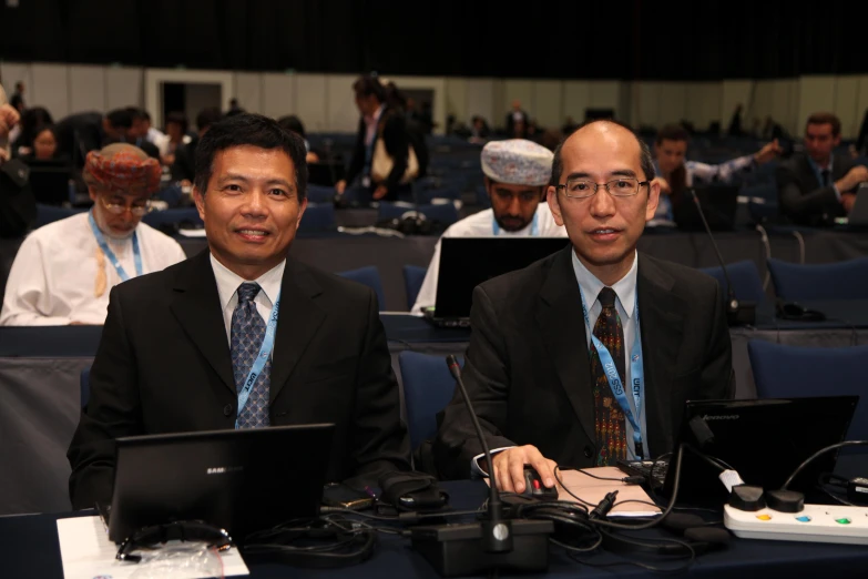 two men sitting next to each other in front of laptop computers