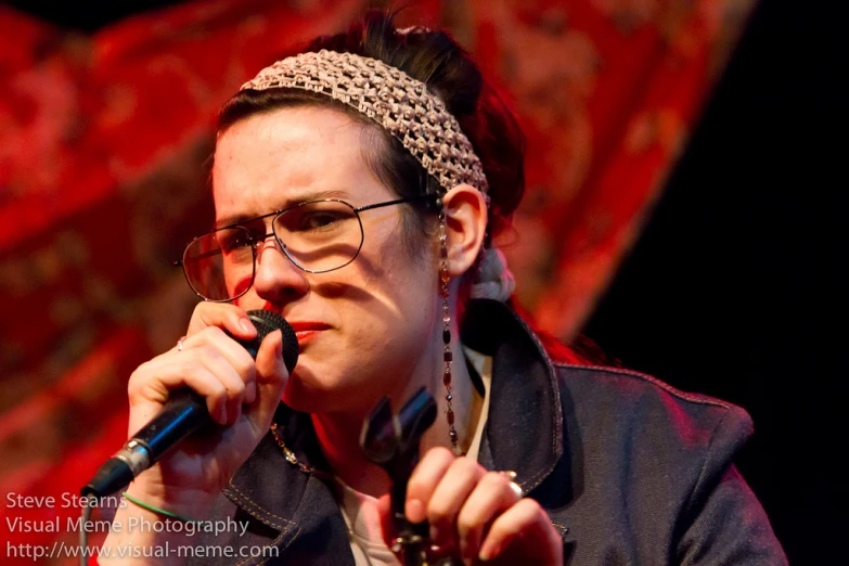 a woman with glasses on singing into a microphone