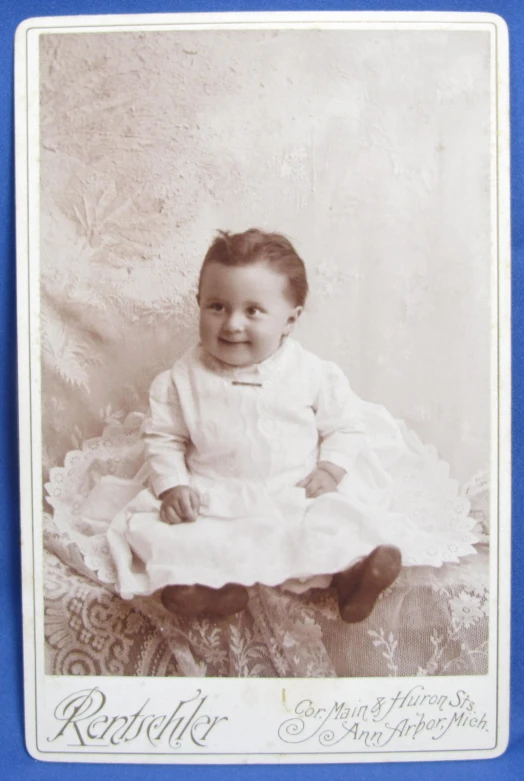 vintage pograph of smiling baby in white gown on a couch