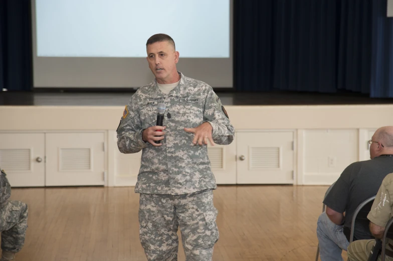 soldier speaking with large audience in background at indoor event