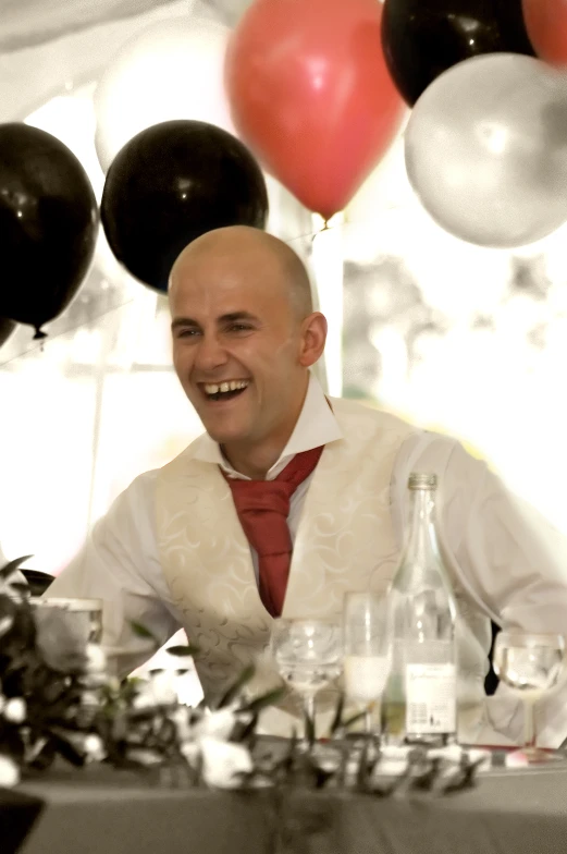 man smiling while sitting at a table with bottles of alcohol