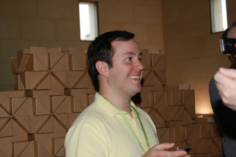 a man wearing glasses and yellow shirt smiling and holding cell phone