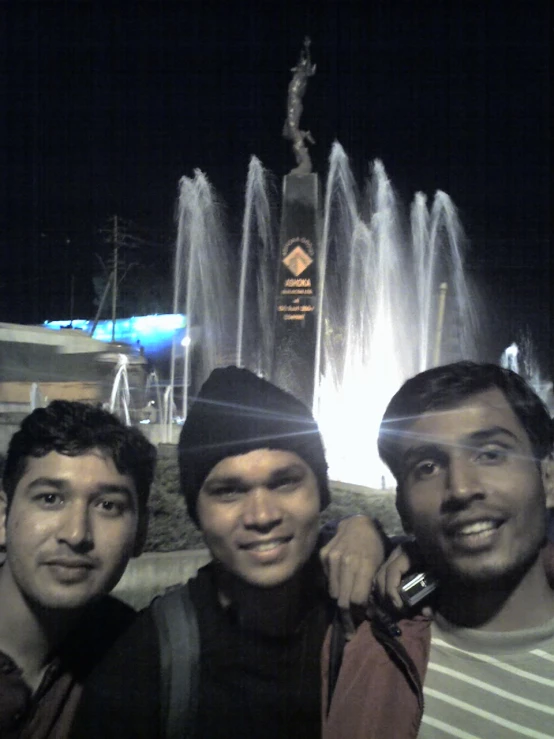 two men standing next to a man in front of a fountain