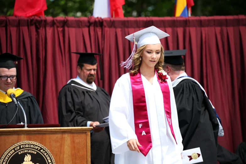 a woman in graduation gown with her diploma on at podium