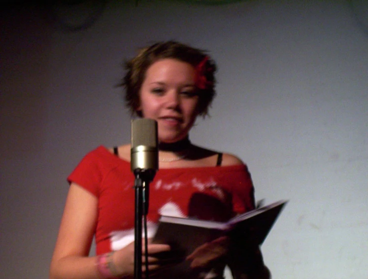 a young woman singing into a microphone while reading a book