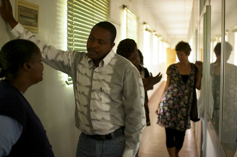 a man in white shirt holding a black object and looking at people walking down the hallway