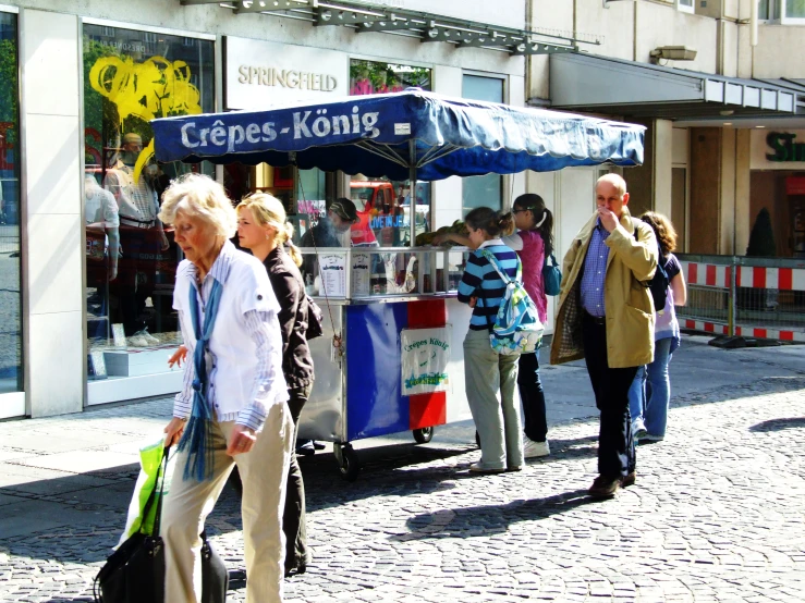 group of people walking down the street in front of a kiosk