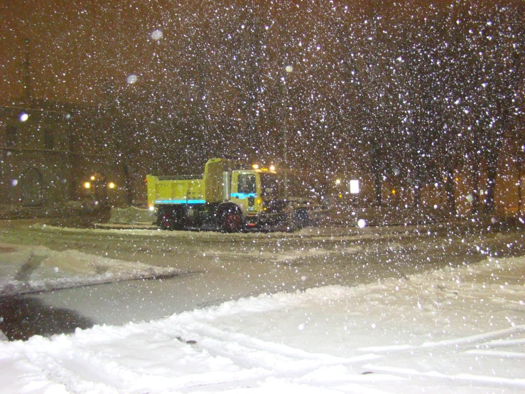 a yellow truck and some cars are outside in the snow